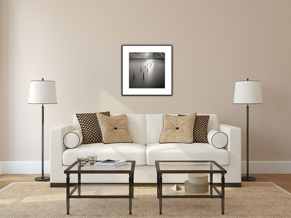 A simple black and white square framed photo of a ghost bird resting on a piling as sunrays gently bathe it fits the warm tones of this living area.