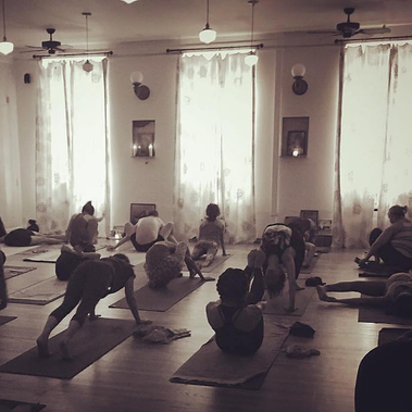 Yoga students practicing in a studio with tall windows.