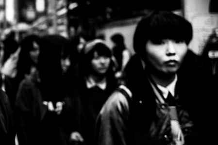 Faces move along Takeshita Street, Harajuku, Tokyo. 
From the photographic series "In Praise of Shadows". Shot on black and white film by photographer Matthew Fleming. 
