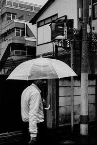 A figure holding an umbrella walks the backstreets of Okubo, Shinjuku, Tokyo. 
From the photographic series "In Praise of Shadows". Shot on black and white film by photographer Matthew Fleming. 