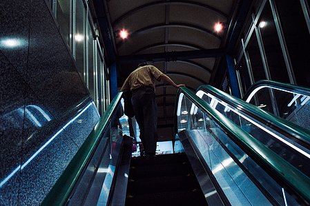 A man reaches the top of an escalator in Tokyo. 
Photograph from the series Forbidden Colours by Matthew James Fleming. Taken with a Leica M6 and Cinestill 800T.