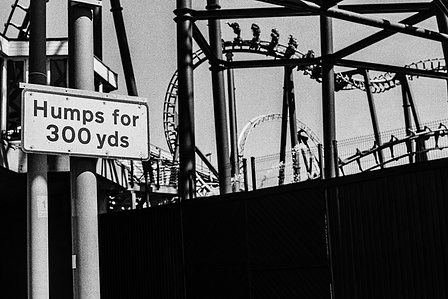 Photograph from the series To Live and Die in Lancashire: The Chapel of the Roses by Matthew James Fleming. Taken with a Leica M6 and Ilford HP5 35mm film.
A sign declares "Humps for 300 yds" with Blackpool Pleasure Beach rollercoaster in view.