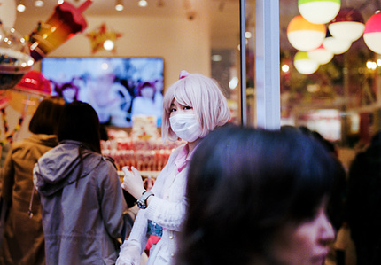 A figure with pink hair wearing a protective facemask whilst walking down Takeshita Street Harajuku, Tokyo. Photograph taken by Matthew Fleming with a Leica M6 and Kodak Portra 400. 