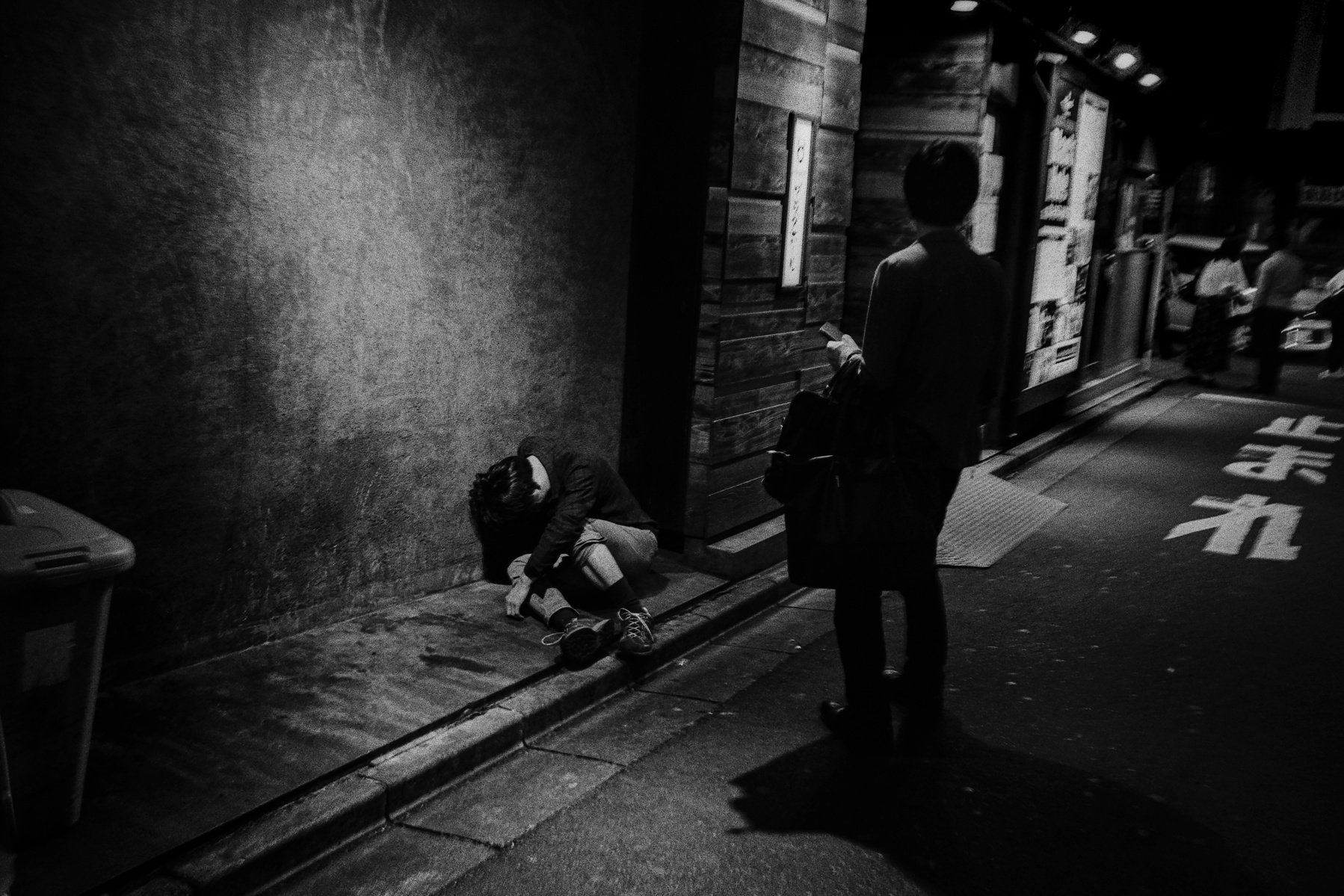 A man sleeps by the side of the road in Shinjuku, Tokyo, June 2018. Photographed by Matthew Fleming on 35mm Ilford HP5 film with a Leica M6.