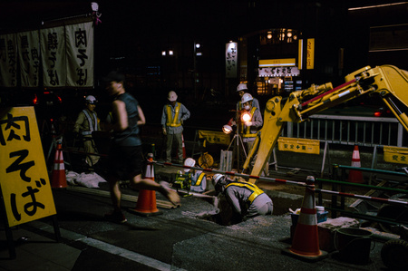 A man runs past a group of workers performing gas maintenance at night. Tokyo. 
Photograph from the series Forbidden Colours by Matthew James Fleming. Taken with a Leica M6 and Kodak Portra 400.