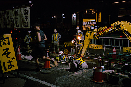 A man runs past a group of workers performing gas maintenance at night. Tokyo. 
Photograph from the series Forbidden Colours by Matthew James Fleming. Taken with a Leica M6 and Kodak Portra 400.