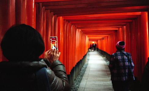 A tourist frames a photograph on a phone of the famous Fushimi Inari Torii, part of a larger shrine complex. Photograph taken by Matthew Fleming with a Leica M6 and Kodak Portra 400 film.