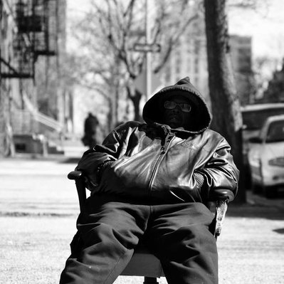 Black and white street photography of the french street photographer David Décamps representing a man sitting and sleeping in a chair in the middle of the street in New York City, USA.