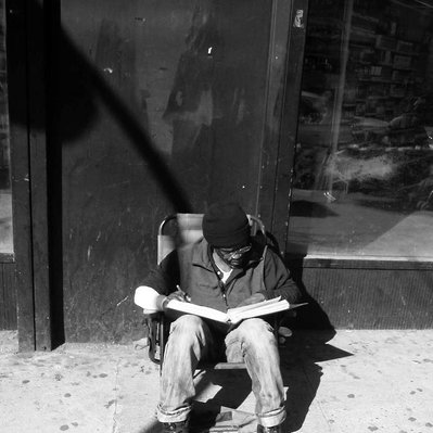 Black and white street photography of the french street photographer David Décamps representing a homeless man reading a book in New York City, USA.