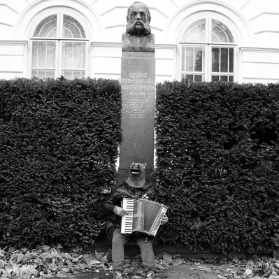 Black and white street photography of the french street photographer David Décamps representing a man playing accordion with a mask of a horse in Vienna.