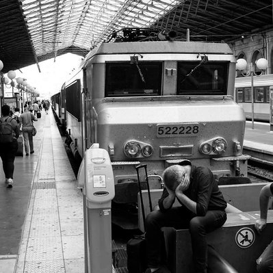 Black and white street photography of the french street photographer David Décamps representing a man head down in his hands in the train station in Paris.