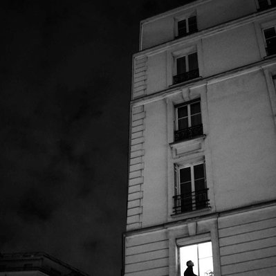 Black and white street photography of the french street photographer David Décamps representing a man smoking alone at his window during the night in Paris.