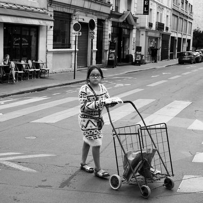 Black and white street photography of the french street photographer David Décamps representing a girl with an empty supermarket trolley in Paris.