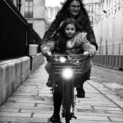 Black and white street photography of the french street photographer David Décamps representing a mum with her daughter on a bike in Paris, France.
