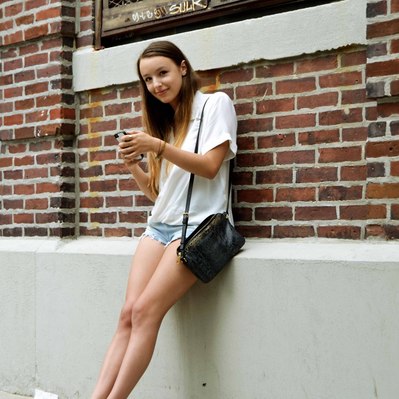Street photography in colors of the french street photographer David Décamps representing a girl leaned on a brick wall with a smile in New York City, USA.