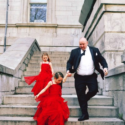 Street photography in colors of the french street photographer David Décamps representing a dad with his two daughters with red dresses in a wedding in Montréal.
