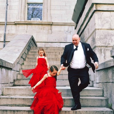 Street photography in colors of the french street photographer David Décamps representing a dad with his two daughters with red dresses in a wedding in Montréal.