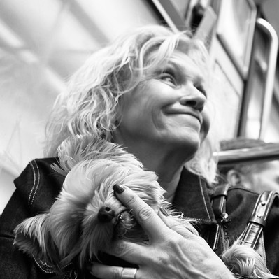 Black and white street photography of the french street photographer David Décamps representing an old woman putting her finger in the eye of her dog in a subway in Paris.