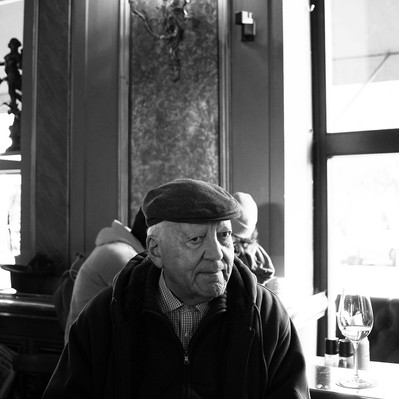 Black and white street photography of the french street photographer David Décamps representing the portrait of an old man at a bar with his glass of white wine in Vienna.