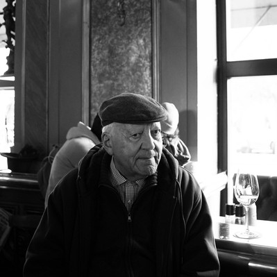 Black and white street photography of the french street photographer David Décamps representing the portrait of an old man at a bar with his glass of white wine in Vienna.