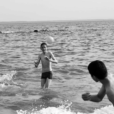 Black and white street photography of the french street photographer David Décamps representing three kids playing in the ocean in Coney Island, New York City, USA.