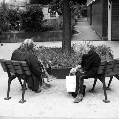 Black and white street photography of the french street photographer David Décamps representing two woman on a bench with a pigeon on her foot in Paris.