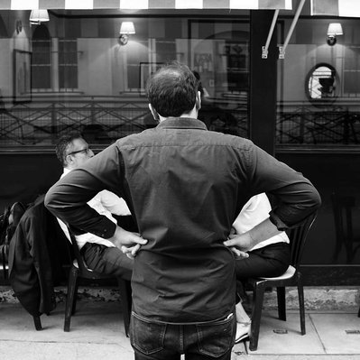 Black and white street photography of the french street photographer David Décamps representing the back of a waiter with his arms on his hips in Paris.