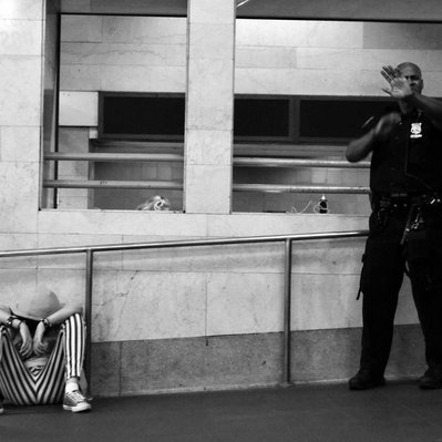 Black and white street photography of the french street photographer David Décamps representing a policeman protecting a young lady in the subway in New York City, USA.
