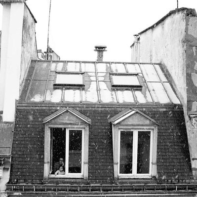 Black and white street photography of the french street photographer David Décamps representing a baby discovering the snow from the window in Paris.