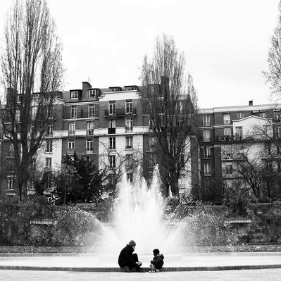 Black and white street photography of the french street photographer David Décamps representing a mum with her child together near a fountain in Paris.