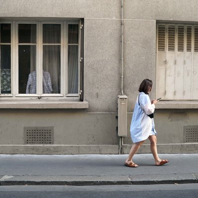 Street photography in colors of the french street photographer David Décamps representing a woman walking on a sidewalk and a shirt hanged at a window in Paris.