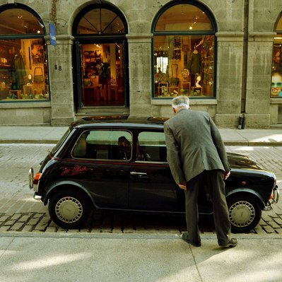 Street photography in colors of the french street photographer David Décamps representing a man looking inside a Mini Cooper car in Montréal.
