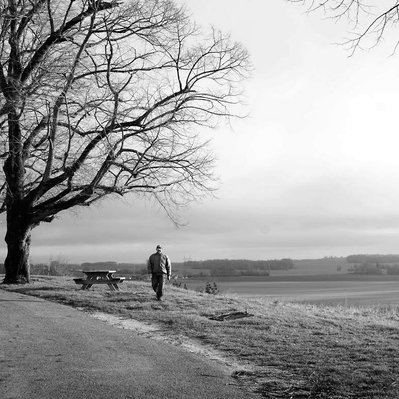 Black and white street photography of the french street photographer David Décamps representing a man walking in the campaign in Doue.