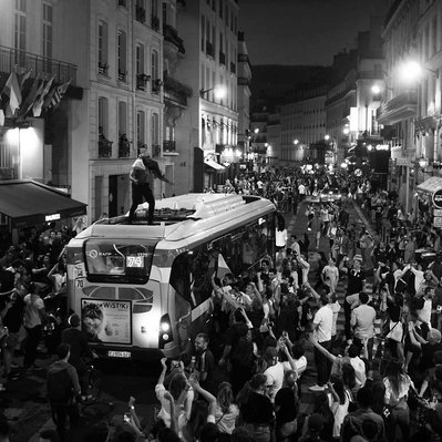 Black and white street photography of the french street photographer David Décamps representing a man up on a bus with a crowd around him during the world cup in Paris.
