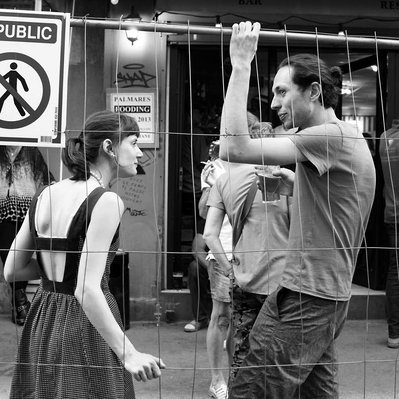 Black and white street photography of the french street photographer David Décamps representing a woman and a man talking behind a grid in Paris.