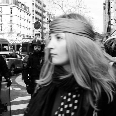 Black and white street photography of the french street photographer David Décamps representing a young woman walking in front of policemen in Paris during a strike.