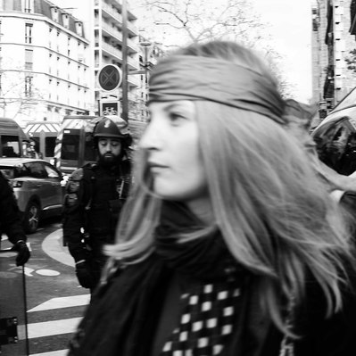 Black and white street photography of the french street photographer David Décamps representing a young woman walking in front of policemen in Paris during a strike.