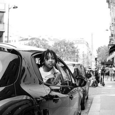 Black and white street photography of the french street photographer David Décamps representing a boy with his head out of a car in Paris.