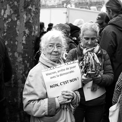 Black and white street photography of the french street photographer David Décamps representing an old woman with a sign during a strike in Paris.