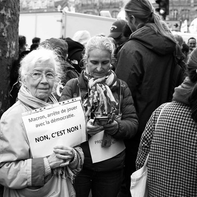 Black and white street photography of the french street photographer David Décamps representing an old woman with a sign during a strike in Paris.
