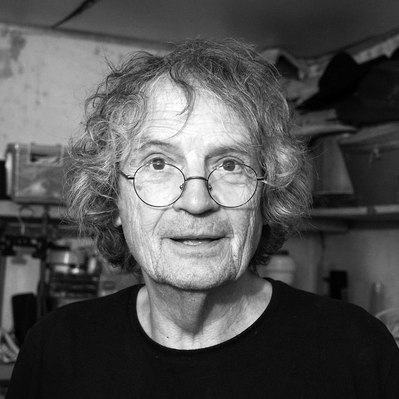 Black and white street photography of the french street photographer David Décamps representing the portrait of an old man with glasses in his atelier in France.