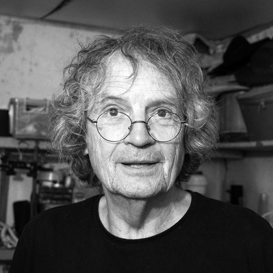 Black and white street photography of the french street photographer David Décamps representing the portrait of an old man with glasses in his atelier in France.