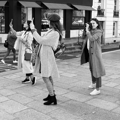 Black and white street photography of the french street photographer David Décamps representing three women taking pictures on a sidewalk in Paris.