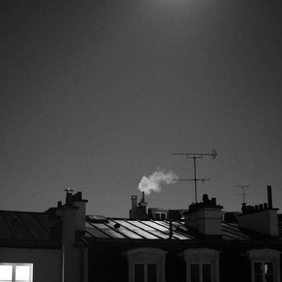 Black and white street photography of the french street photographer David Décamps representing a smoky chimney in the night in Paris.