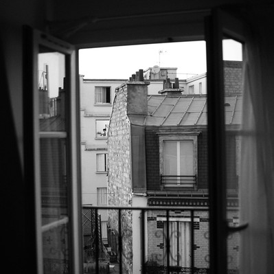 Black and white street photography of the french street photographer David Décamps representing the view of a woman at her window from another window in Paris.