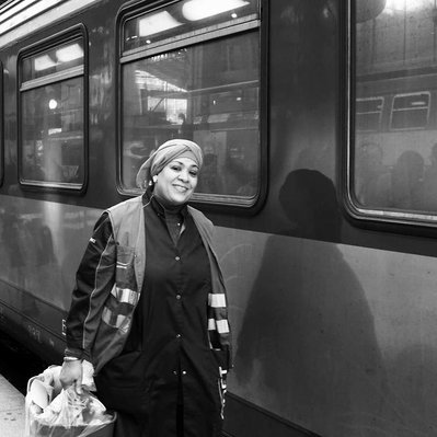 Black and white street photography of the french street photographer David Décamps representing a cleaning lady smiling in a train station in Paris.