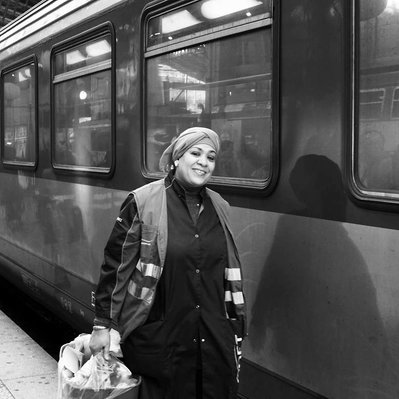 Black and white street photography of the french street photographer David Décamps representing a cleaning lady smiling in a train station in Paris.