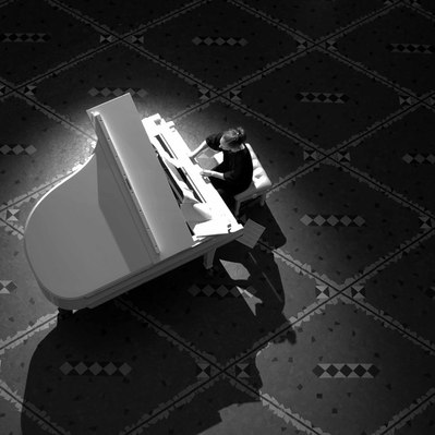 Black and white street photography of the french street photographer David Décamps representing from the top a woman playing piano in a sweet light in Paris.