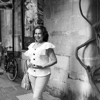 Black and white street photography of the french street photographer David Décamps representing a woman in the sunlight near a bar in Paris.