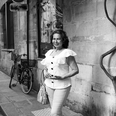 Black and white street photography of the french street photographer David Décamps representing a woman in the sunlight near a bar in Paris.